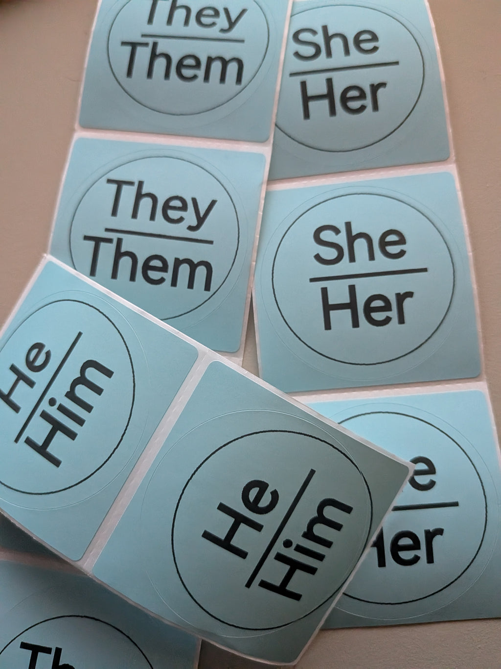 Pronoun stickers showing He/Him, She/Her, and They/Them in a minimalist circle design on blue background