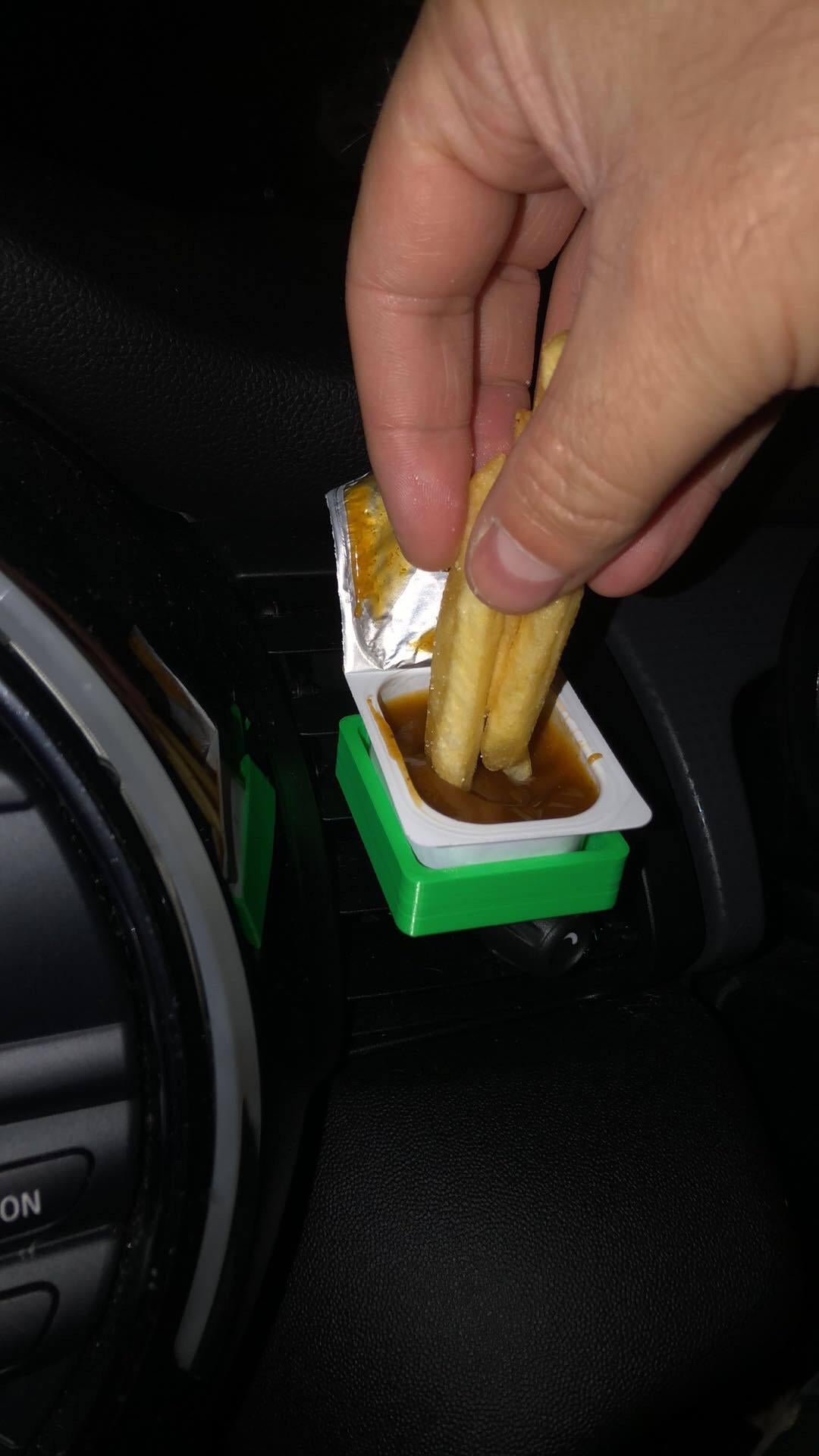 Hand dipping fries into sauce pot held in green 3D printed car vent clip