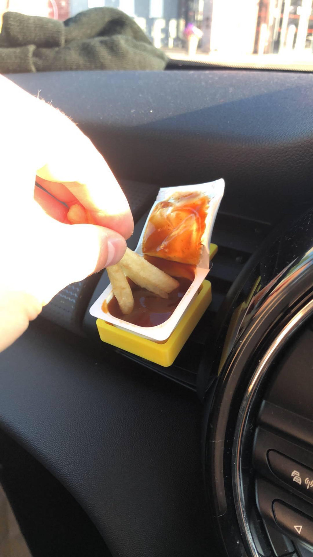 Yellow 3D printed sauce holder on car vent with fries being dipped into ketchup pot